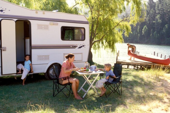 Gezin zit buiten een caravan aan tafel in een groene omgeving.