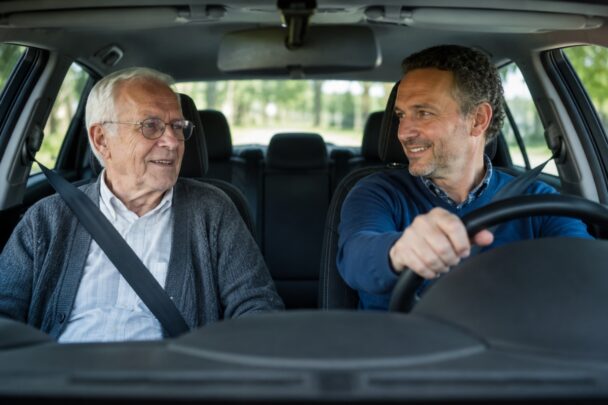 Oudere man wordt als passagier vervoerd in een auto door een man van middelbare leeftijd.