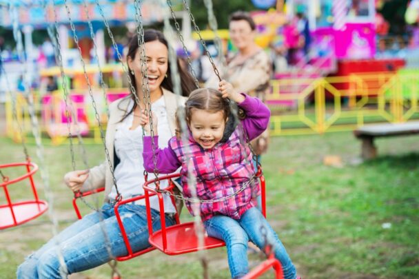 Meisje zit met haar moeder in de zweefmolen op de kermis.