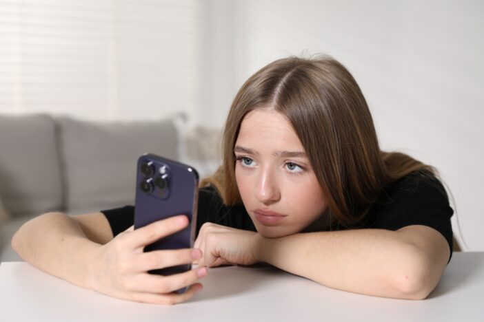 Tienermeisje kijkt bedrukt naar haar smartphone.