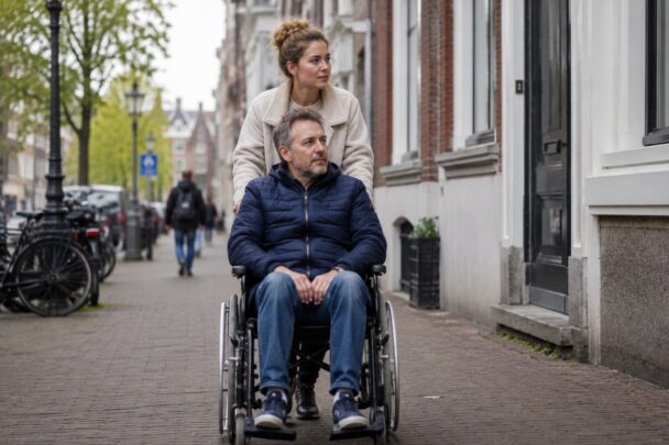 Vrouw duwt man voort in rolstoel, in de stad.