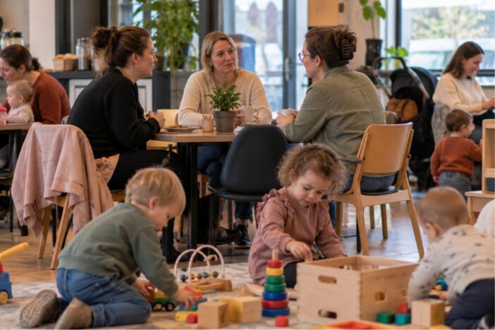 Moeders praten samen in café terwijl kindjes aan het spelen zijn in de speelhoek.